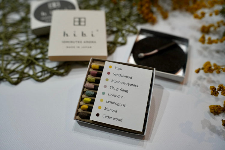 An opened box showing 8 colourful incense match sticks, and an incense burning on a mat in the background.