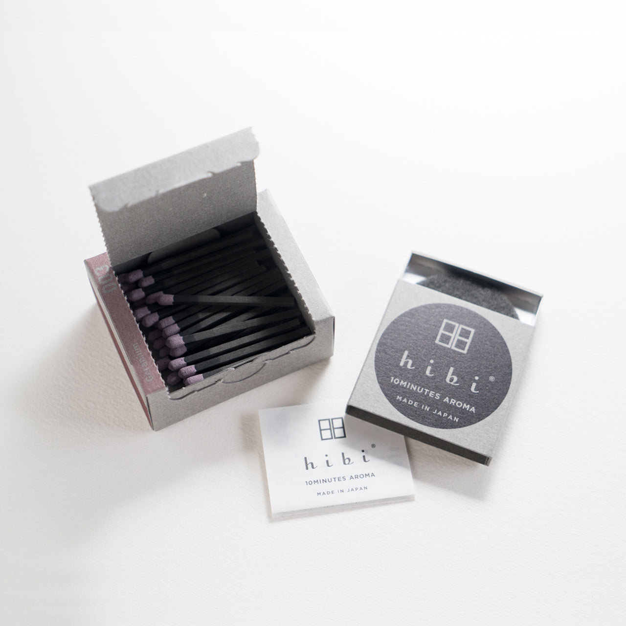 An opened box of Hibi 10 Minutes Aroma Geranium incense matches containing 30 incense sticks with yellow tips. Next to it is a box containing a non-flammable incense mat. All set in a white background.