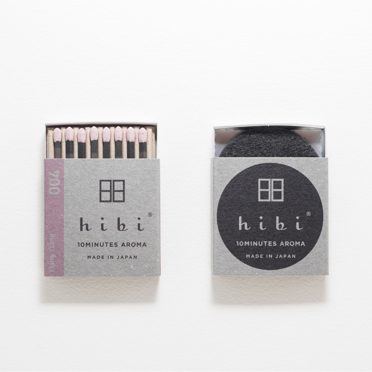 An opened box of Hibi 10 Minutes Aroma Ylang Ylang incense matches containing 8 incense sticks with light pink tips. Next to it is a box containing a non-flammable incense mat. All set in a white background.