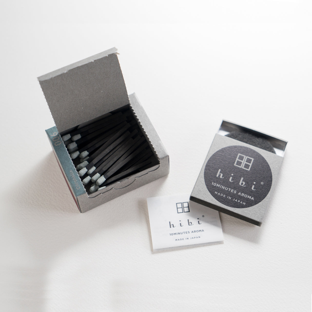 An opened box of Hibi 10 Minutes Aroma Citronella incense matches containing 30 incense sticks with yellow tips. Next to it is a box containing a non-flammable incense mat. All set in a white background.