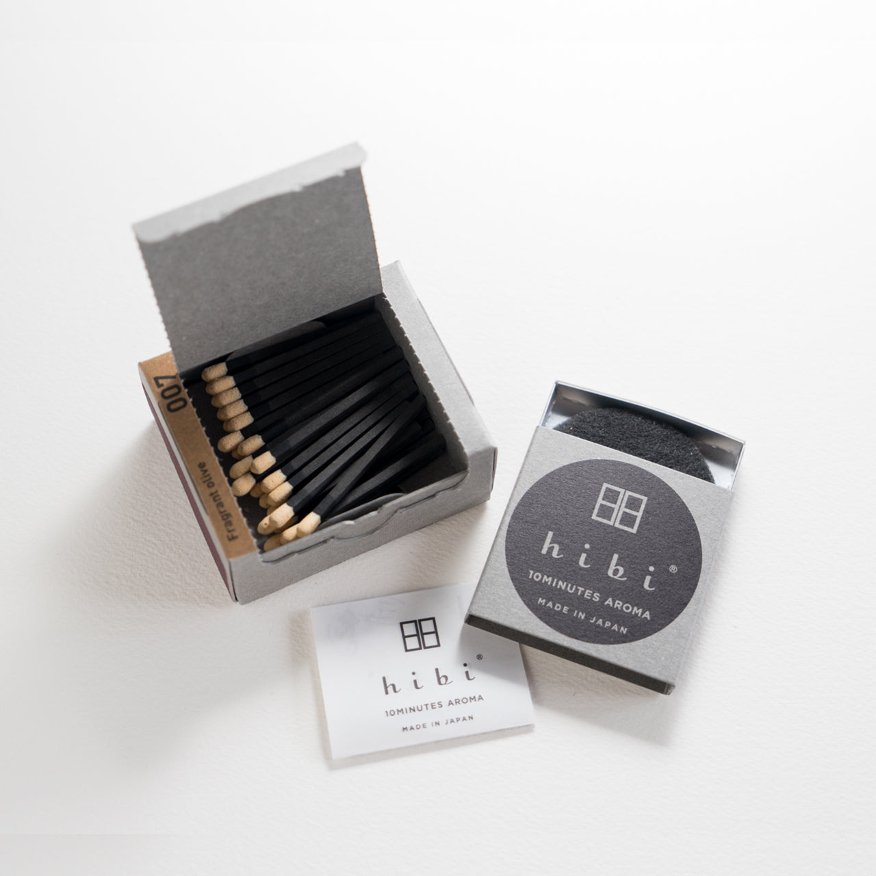 An opened box of Hibi 10 Minutes Aroma Osmanthus incense matches containing 30 incense sticks with yellow tips. Next to it is a box containing a non-flammable incense mat. All set in a white background.