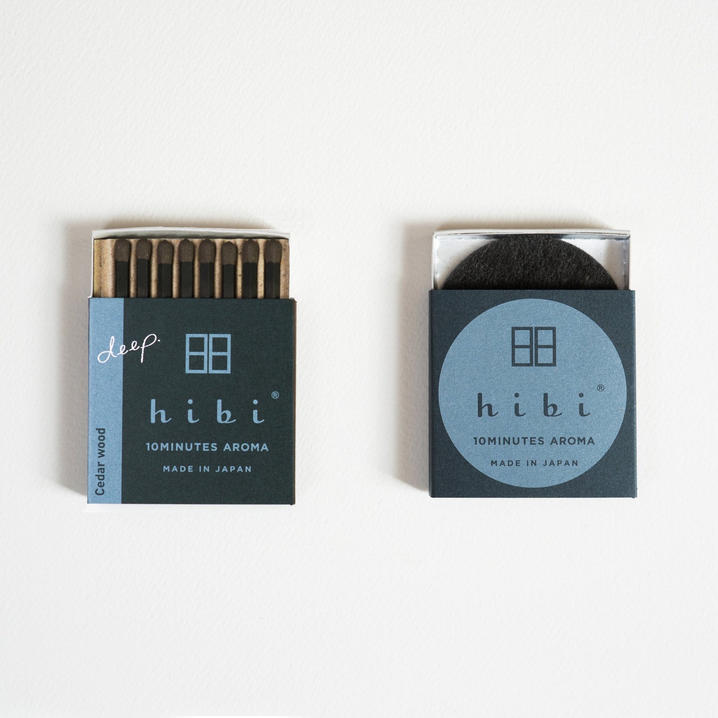 An opened box of Hibi 10 Minutes Aroma Cedar Wood incense matches containing 8 incense sticks with pink tips. Next to it is a box containing a non-flammable incense mat. All set in a white background.