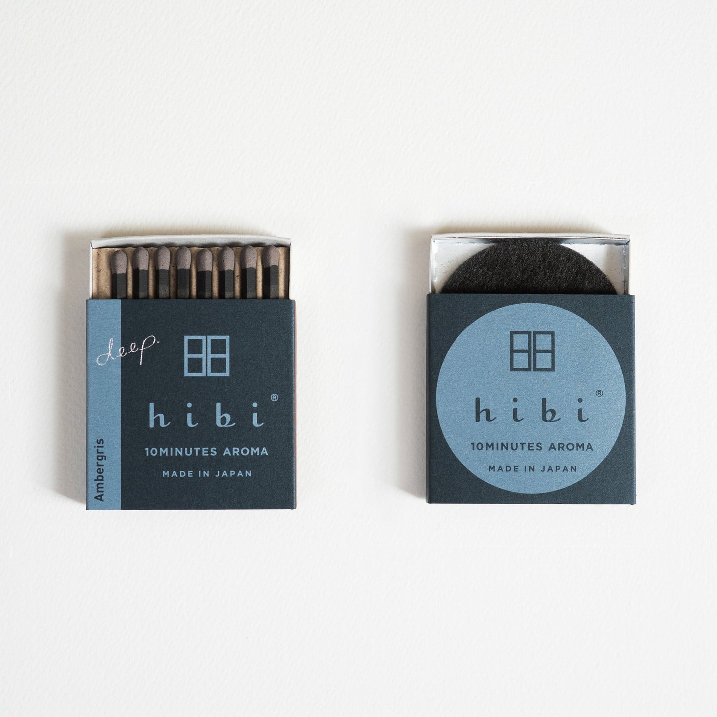 An opened box of Hibi 10 Minutes Aroma Ambergris incense matches containing 8 sticks of incense matches with pink tips. Beside it is a box containing a non-flammable incense mat. All set in a white background.