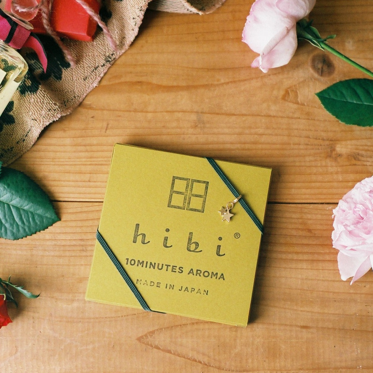 Lying on the top of a wood surface is a Yellow Hibi 10 Minutes Aroma gift box being wrapped with a green ribbon and a golden star charm.