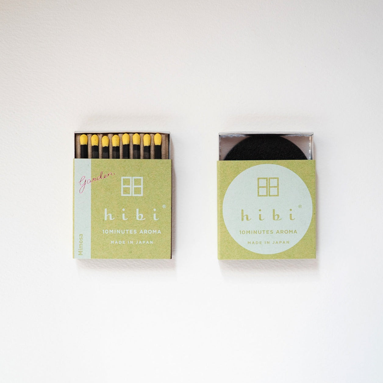 An opened box of Hibi 10 Minutes Aroma Mimosa incense matches which contains 8 incense sticks with yellow tips. Sitting next to it is a box containing a non-flammable mat. All set in a white background.