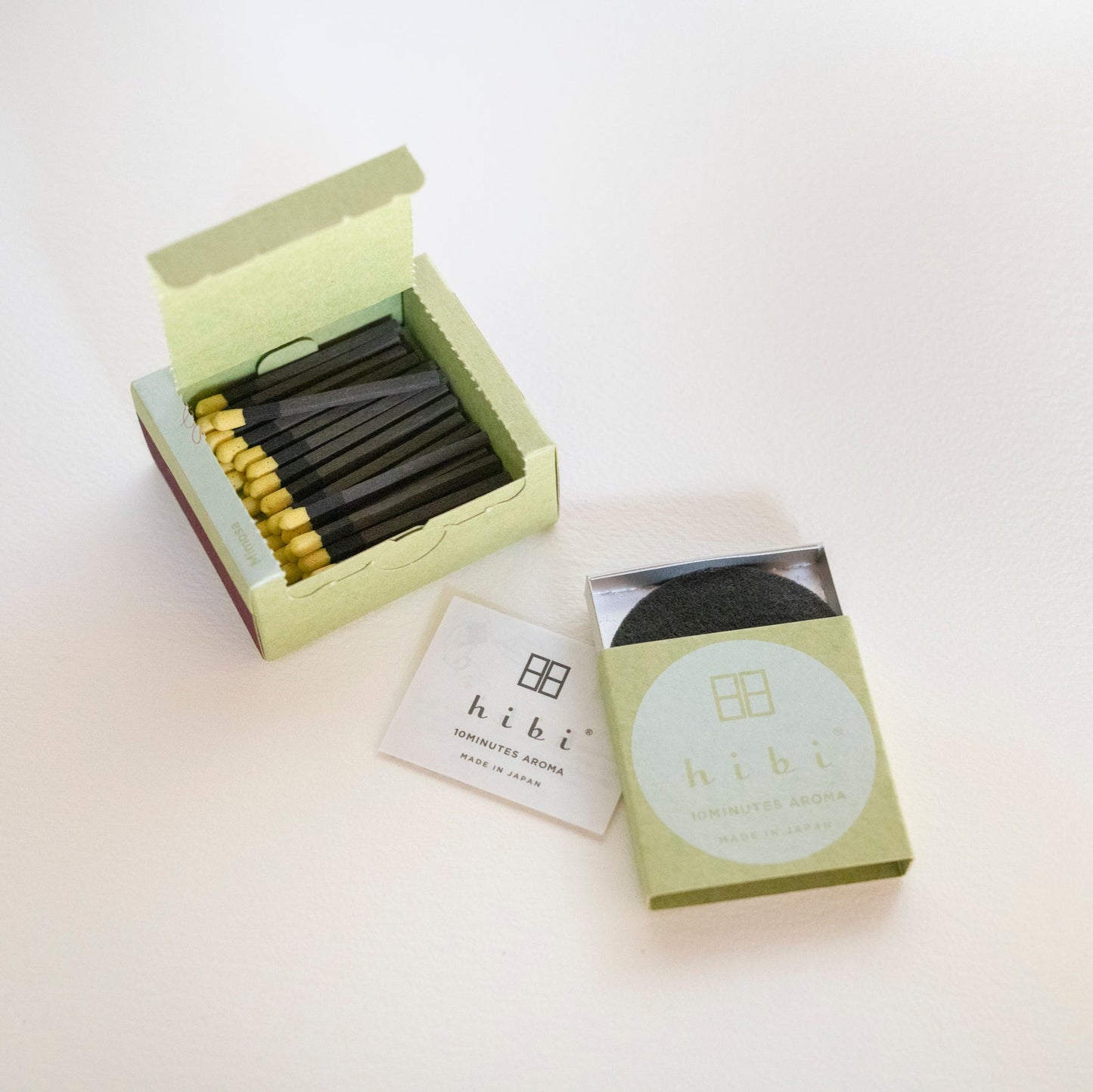 An opened box of Hibi 10 Minutes Aroma Mimosa incense matches containing 30 incense sticks with yellow tips, and a box containing a non-flammable mat. All set in a white background.
