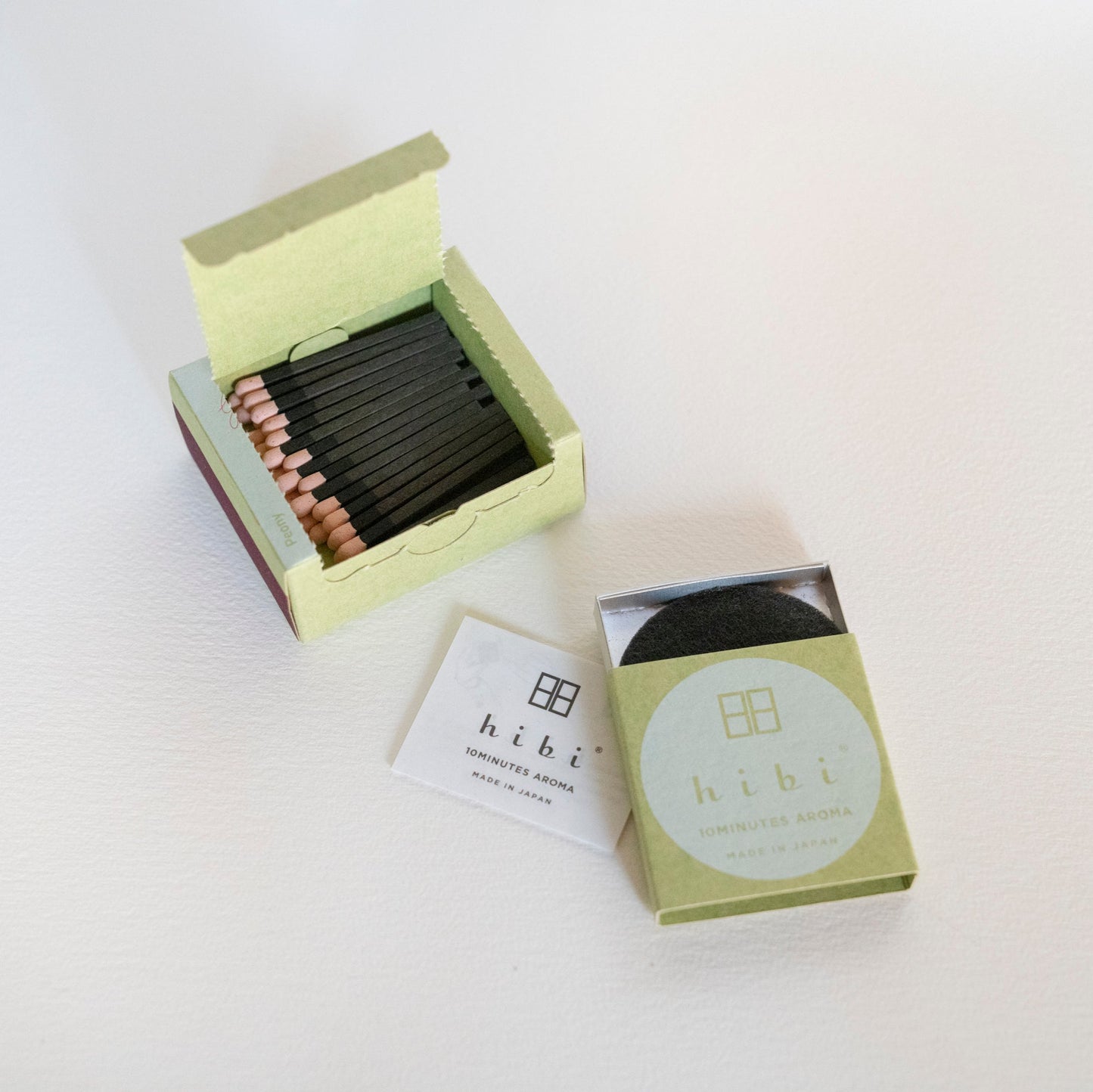 An opened box of Hibi 10 Minutes Aroma Peony incense matches containing 30 incense sticks with pink tips, and a box containing a non-flammable mat. All set in a white background.