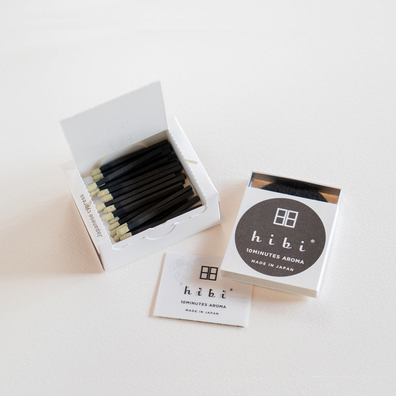An opened box of Hibi 10 Minutes Aroma Japanese Cypress incense matches containing 30 incense sticks with yellow tips, and a box containing a non-flammable mat. All set in a white background.