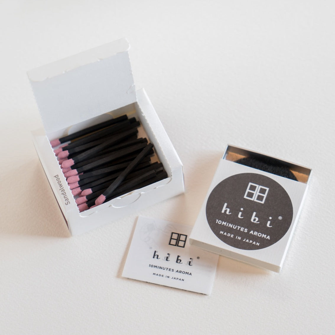 An opened box of Hibi 10 Minutes Aroma Sandalwood incense matches containing 30 incense sticks with pink tips, and a box containing a non-flammable mat. All set in a white background.