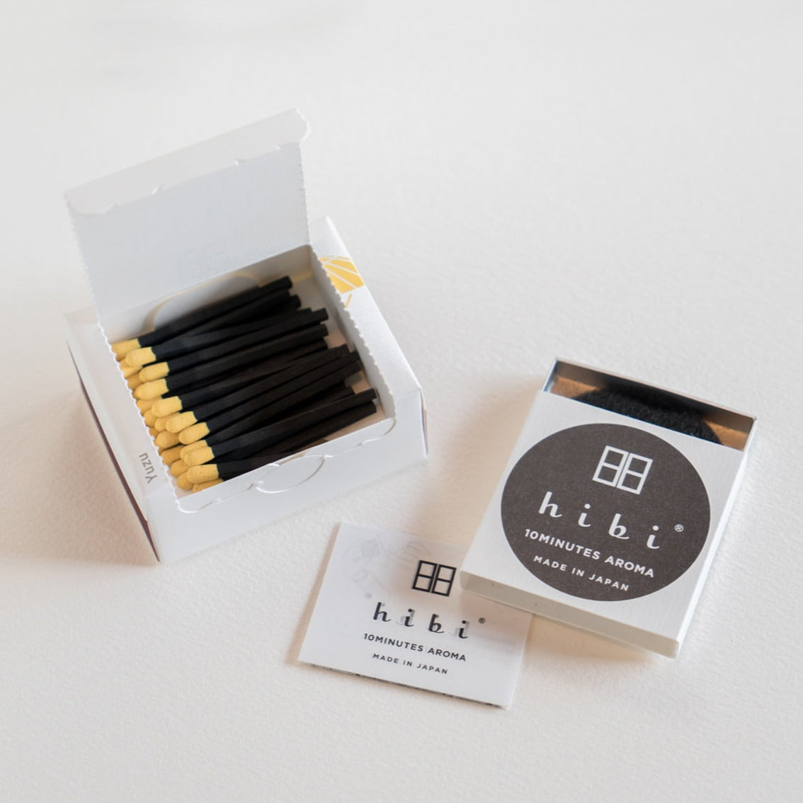AAn opened box of Hibi 10 Minutes Aroma Yuzu incense matches containing 30 incense sticks with yellow tips, and a box containing a non-flammable mat. All set in a white background.