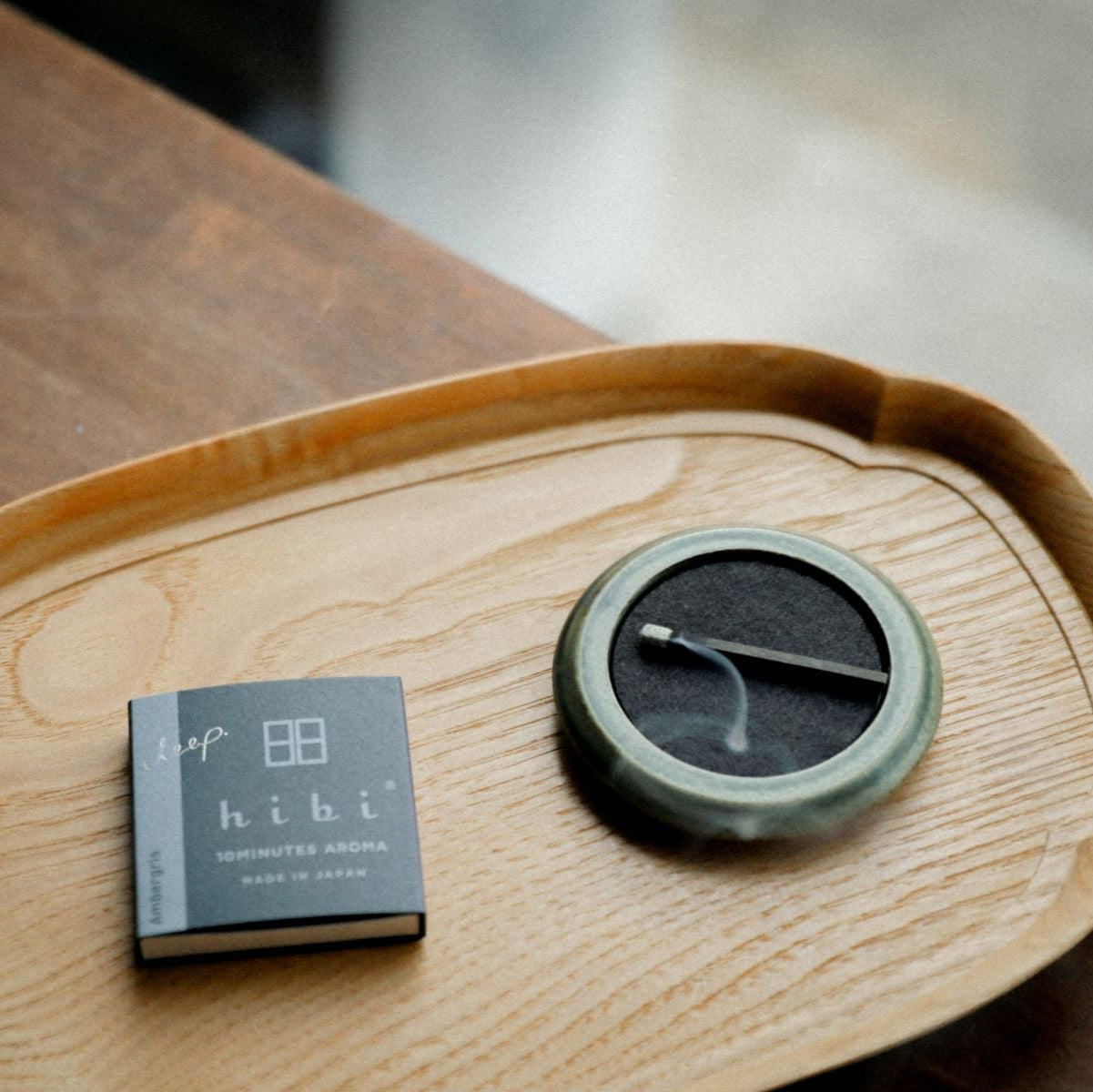 A round green porcelain Seto incense tray in a wooden tray. Next to it is a Hibi 10 Minutes Aroma Deep incense box containing 8 incense sticks.