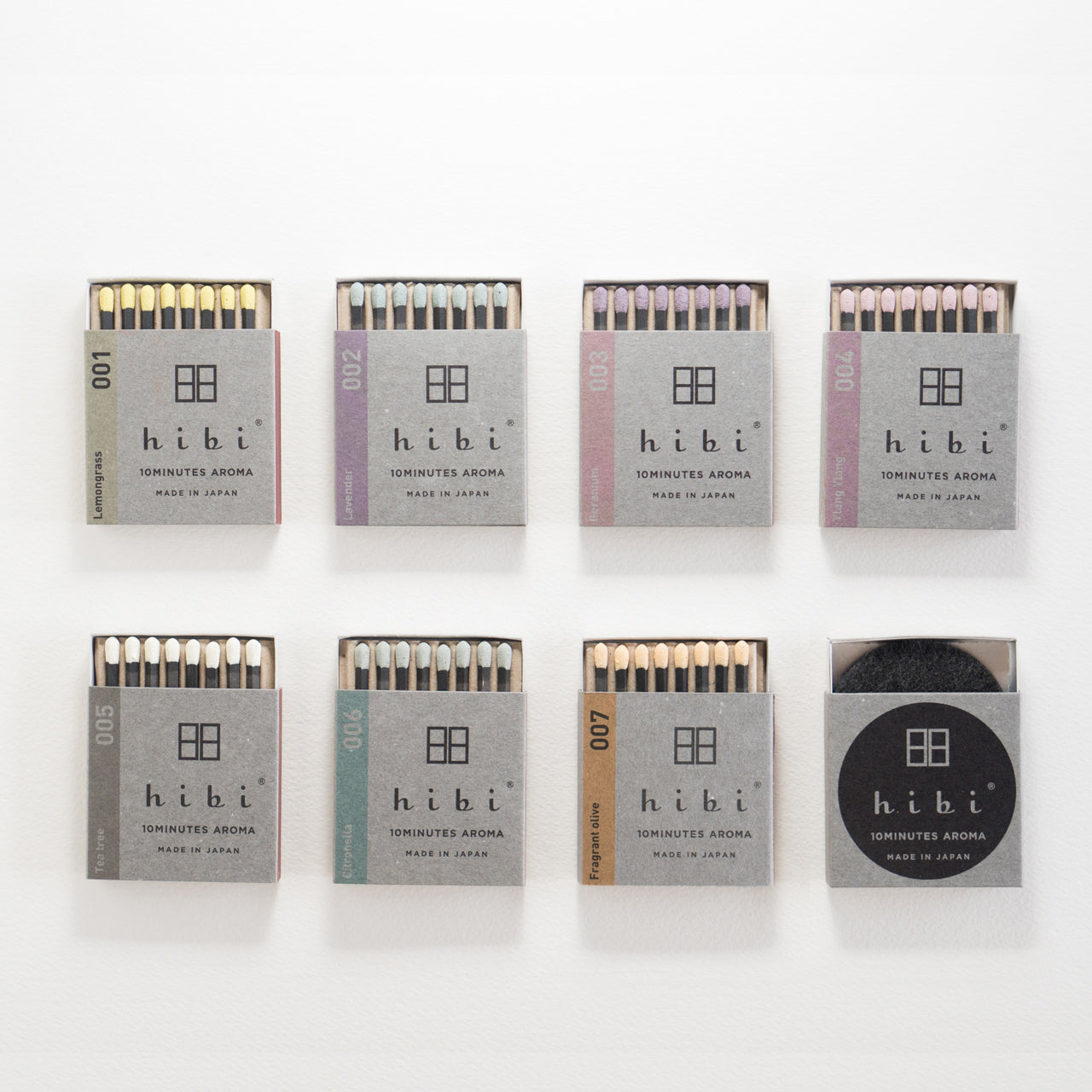 Set on a white background are seven opened box of Hibi 10 Minutes Aroma incense matches each contains 8 sticks of incense matches with colourful tips. There is also a box containing a non-flammable incense mat.